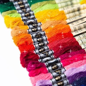 May include: A collection of colorful embroidery floss spools with glitter thread. The spools are arranged in a rainbow pattern, starting with dark green and ending with a dark blue.