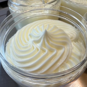 May include: A clear glass jar filled with a white whipped cream-like substance. The cream is swirled and has a smooth, creamy texture.