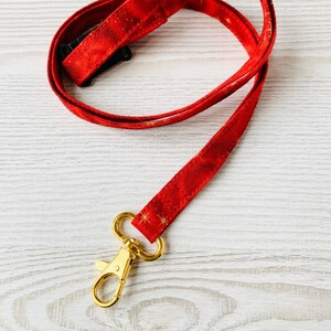 Op de afbeelding: Een rode lanyard met gouden glittersterren en een gouden metalen clip.