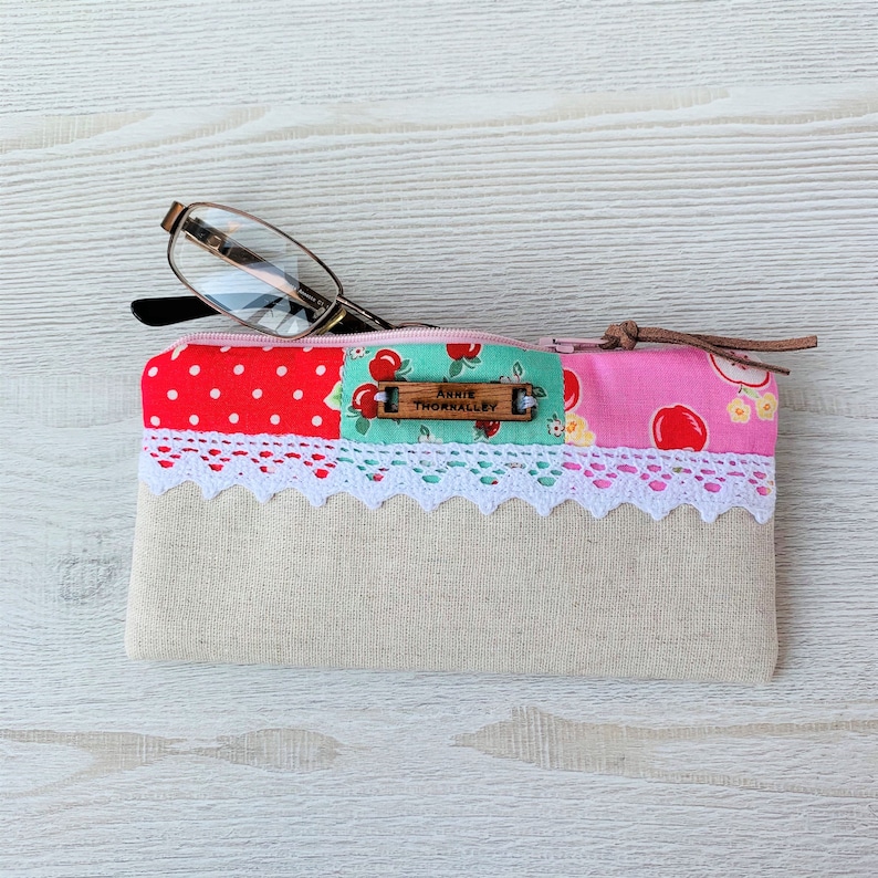 May include: A pink and red patchwork fabric zippered pouch with a white lace trim and a wooden tag that reads "Annie Thornalley".