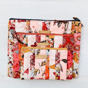 May include: Three pink and orange floral fabric zippered pouches with a navy blue zipper on the largest pouch. Each pouch has a brown label with the text "Annie Thornalley" printed on it.