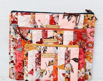 Puede incluir: Tres bolsas de cremallera de tela floral rosa y naranja con una cremallera azul marino en la bolsa más grande. Cada bolsa tiene una etiqueta marrón con el texto "Annie Thornalley" impreso en ella.