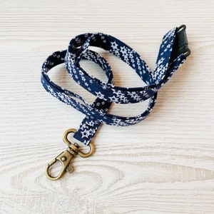 May include: A navy blue lanyard with white stars printed on it. The lanyard has a gold metal clip on one end and a black plastic clip on the other end.