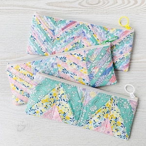 Puede incluir: Tres estuches con cremallera hechos de tela con un diseño de patchwork. Los estuches son en tonos de rosa, verde y blanco con patrones florales.