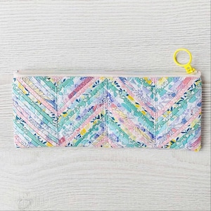 May include: A colorful zippered pouch with a patchwork design of floral fabric in shades of pink, blue, green, and white. The pouch has a yellow zipper pull.