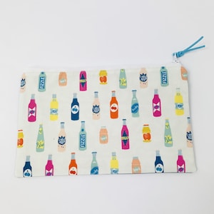Könnte beinhalten: Eine weiße Reißverschlusstasche mit einem bunten Muster aus Sodaflaschen. Die Flaschen haben verschiedene Geschmacksrichtungen, darunter Zitrone, Kirsche und Blaubeere. Die Tasche ist perfekt zum Verstauen von kleinen Gegenständen wie Make-up, Stiften oder Bleistiften.