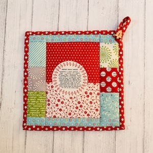 Puede incluir: Un agarrador de olla de patchwork rojo, blanco y verde con una receta de galletas de azúcar impresa en él. El agarrador de olla tiene un borde rojo y una etiqueta de madera con el número 4.