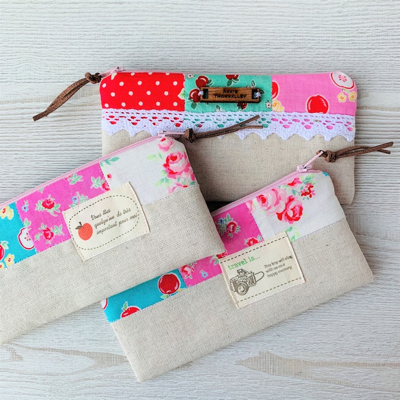 May include: Three pink and white patchwork fabric pouches with zipper closures. The pouches have different designs and include the text "Travel is... This trip with a long with a happy memory" and "Dress what you enjoy, no matter what is important for me".