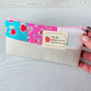 May include: A pink and blue patchwork fabric pencil case with a zipper closure. The case has a white label with a red apple and the text "Vous &ecirc;tes quelqu'un de tr&egrave;s important pour moi".