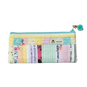 Op de afbeelding: Een lichtblauwe rits-tas met een patchwork-ontwerp gemaakt van verschillende kleurrijke stoffen. De tas heeft een klein label met de tekst "hand made" en "Easter Egg Hunt by N."