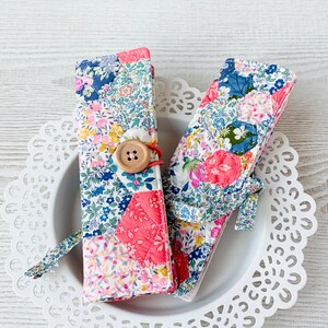 May include: Two fabric pencil cases with a patchwork design in shades of pink, blue, and white. The cases have a button closure and are made of a quilted fabric.