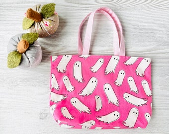 May include: A pink tote bag with white ghost illustrations. The bag has pink handles and is made of a canvas material.