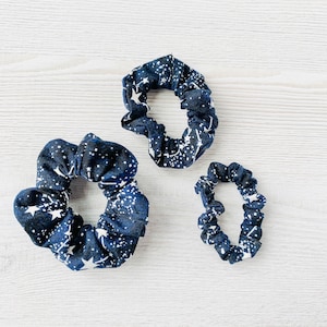 May include: Three navy blue scrunchies with a white star pattern. The scrunchies are different sizes.