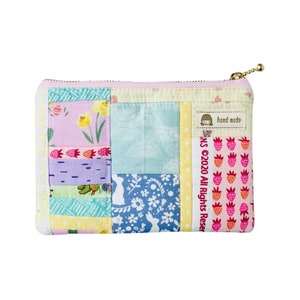 May include: A patchwork fabric zippered pouch with a pink, yellow, blue, and green colour scheme. The pouch has a zipper closure and a small tag that says "hand made".
