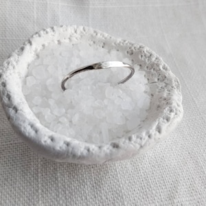 Peut inclure: Une bague en argent martelée posée sur un plat en céramique blanche rempli de cristaux de sel blanc.