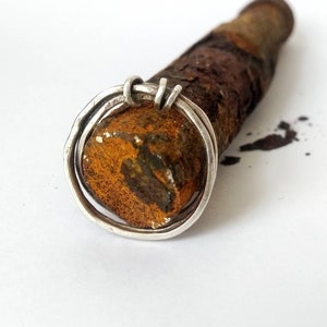 Può includere: Un anello d'argento con un design a doppia fascia, avvolto attorno a un pezzo di metallo arrugginito.