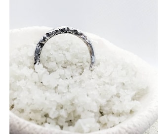 May include: A silver ring with a textured surface, resting on a bed of white salt crystals.