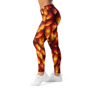 Pode incluir: Leggings justas com um padrão vibrante de penas em tons de laranja, amarelo e bordô. As leggings são usadas com tênis brancos. O design cria um efeito artístico e ardente.