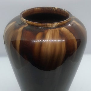 May include: A brown and cream glazed ceramic vase with a rounded bottom and a wide opening. The vase has a streaky glaze pattern.