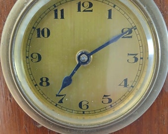 May include: A wooden clock with a carved leaf design. The clock face is brass with black Roman numeral hour markers and black hands.