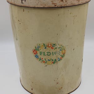 May include: A vintage, off-white metal canister with a floral design and the word "FLOUR" printed on the front. The canister has a slightly rusted appearance.