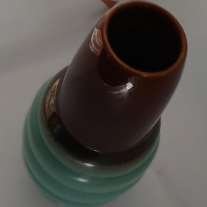 May include: A brown and green ceramic vase with a wide opening. The vase has a rounded, bulbous base and a cylindrical neck.