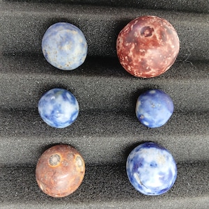 May include: Six spherical stones in blue and brown hues. The stones have a smooth, polished finish, with diverse colours and textures. The arrangement includes a mix of solid and patterned stones, displaying natural variations.