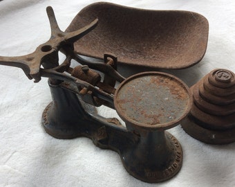 May include: Vintage cast iron kitchen scale with a rusty brown finish. The scale has a round platform and a scoop-shaped pan. A set of rusty weights are also included.