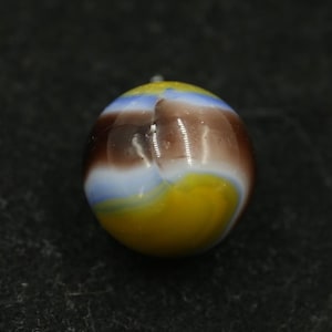 May include: A colorful glass marble with a swirl pattern. The marble features a combination of yellow, brown, blue, and white colors. The marble is round and has a glossy finish. This collectible item is suitable for games or display.