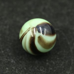 Peut inclure: Bille vintage avec une base vert clair, ornée de motifs tourbillonnants marron foncé et noirs. La sphère de verre a une finition brillante. Un jouet ou objet de collection classique, sur fond sombre.