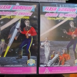 May include: Two vintage VHS tapes of "Flash Gordon Conquers the Universe" starring Buster Crabbe. The covers feature a space-themed illustration with a man in a red shirt and blue pants, holding a ray gun. Volume One and Four are visible.