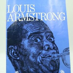 May include: A book cover with a blue illustration of Louis Armstrong playing a trumpet. The title "LOUIS ARMSTRONG" is printed in white block letters at the top. The image is set against a light blue background.