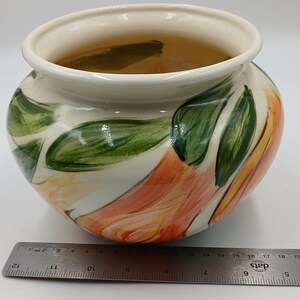 May include: A white ceramic pot with a hand-painted design of orange and yellow flowers with green leaves.