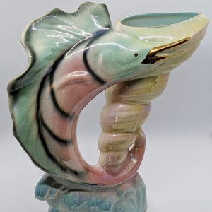 May include: A ceramic vase shaped like a stylised fish with a green, pink and yellow glaze. The fish is curled into a circle with its tail raised. The vase has a gold accent on the fish's fin.
