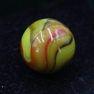 May include: A colorful glass marble with a swirl pattern. The marble features a mix of yellow, red, and brown colors. The glass is translucent, allowing light to pass through, and has a glossy finish. The marble is a sphere.