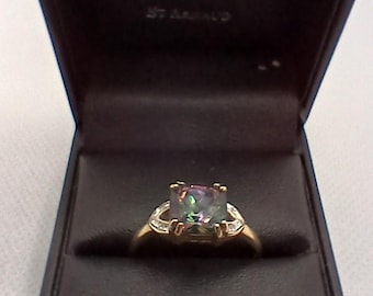 May include: A gold ring with a large, square-shaped, iridescent gemstone set in the center. The ring is in a black velvet ring box with the words "Gold 'N Silver Mine" and "Jewellers" printed on the inside of the lid.