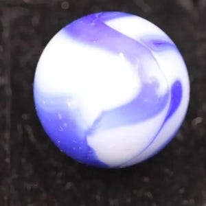 Peut inclure: Gros plan sur une bille de verre avec un motif tourbillonnant de blanc et de violet. La bille est ronde et lisse, avec les couleurs se fondant les unes dans les autres. Un jouet classique, aux couleurs vives.