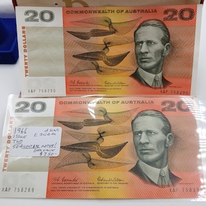 May include: Two Australian twenty-dollar banknotes. The notes feature a portrait of a man and a design of stylized birds. The text "TWENTY DOLLARS" is visible. One note has a sticker with text.