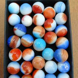 May include: A selection of colourful marbles in a black tray. The marbles display a variety of colours, including blue, orange, red, and white, with swirled and striped patterns. The marbles are round and appear to be made of glass.