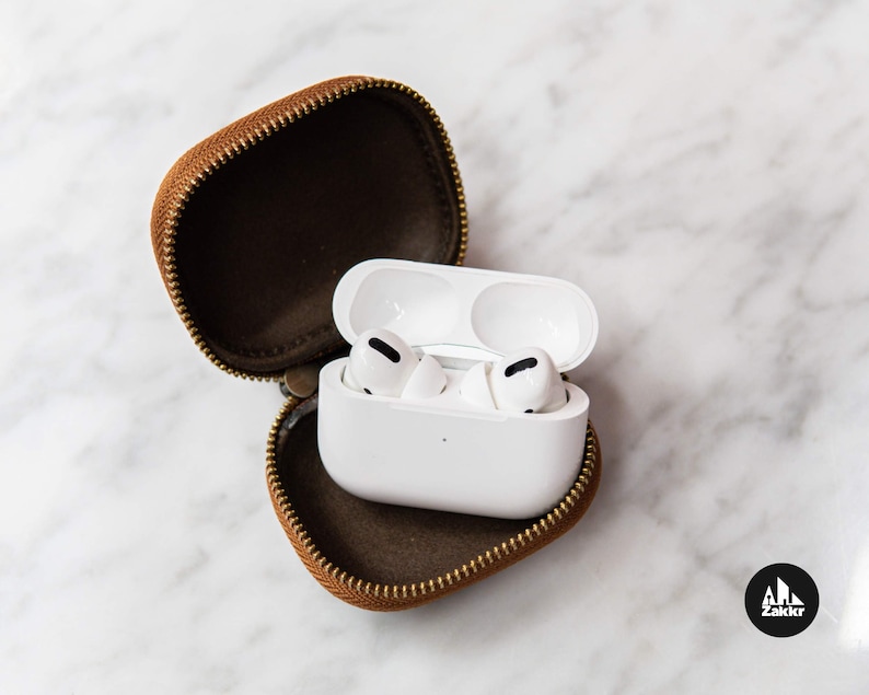 May include: White wireless earbuds in a brown leather case with a zipper. The earbuds are in their charging case.