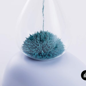 K&ouml;nnte beinhalten: Eine gl&auml;serne Sanduhr mit blauem magnetischem Sand im Inneren. Der Sand ist zu einer Kugelform zusammengeklumpt.