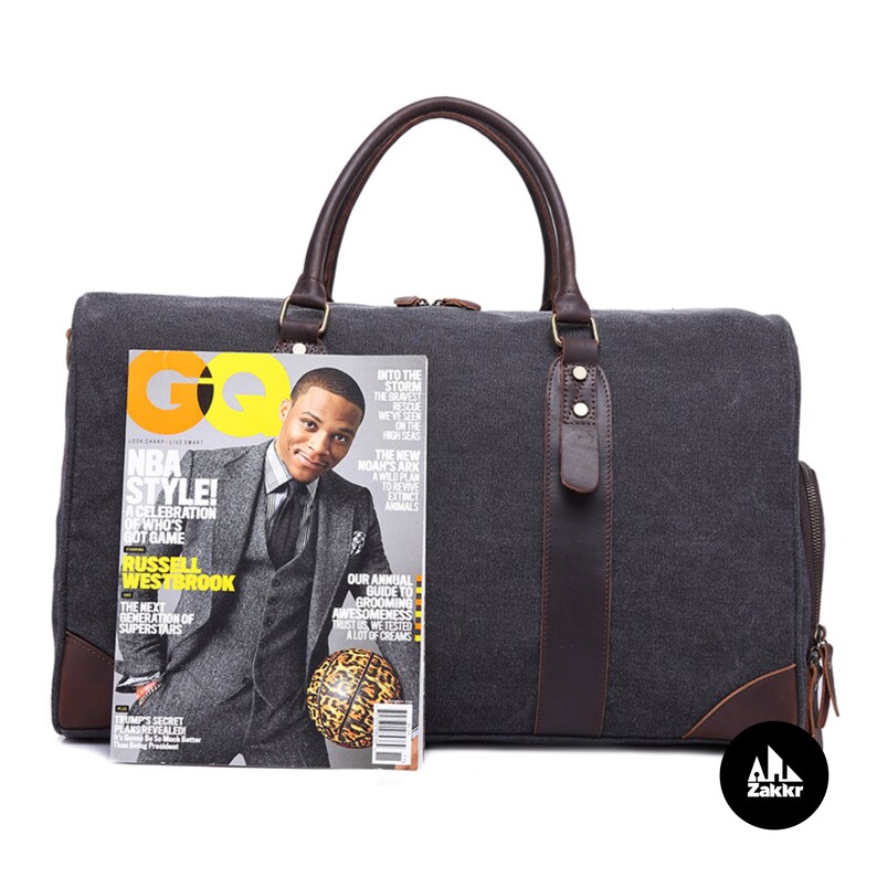 Pu&ograve; includere: Una borsa da viaggio in tela grigia con dettagli in pelle marrone e chiusura a zip. La borsa ha un manico superiore e una tracolla. Una rivista con un giocatore di basket &egrave; davanti alla borsa.
