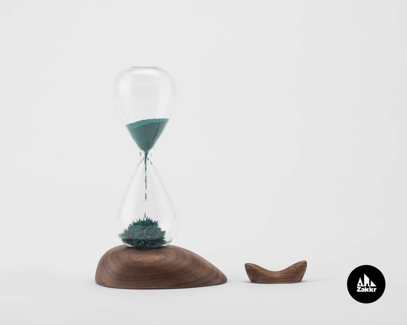 K&ouml;nnte beinhalten: Eine t&uuml;rkisfarbene Sanduhr mit einem Holzsockel und einem separaten Holzst&auml;nder. Die Sanduhr steht auf einem wei&szlig;en Hintergrund. Der Markenname "Zakkr" ist in der unteren rechten Ecke des Bildes sichtbar.