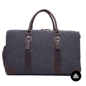 Pu&ograve; includere: Una borsa da viaggio in tela grigia e pelle marrone con dettagli dorati e chiusura a zip. La borsa ha due manici superiori e una tracolla.