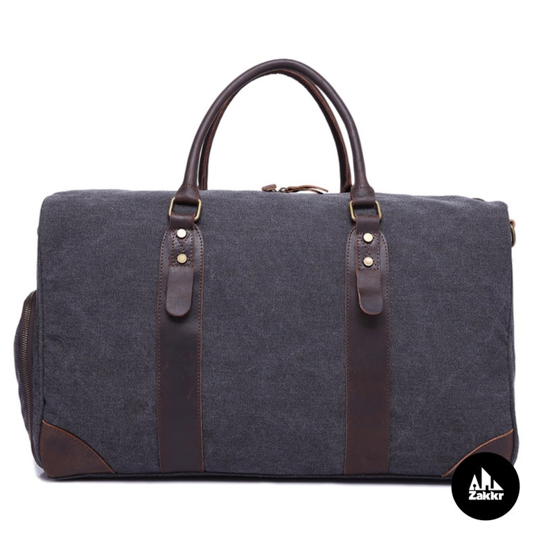 Pu&ograve; includere: Una borsa da viaggio in tela grigia e pelle marrone con dettagli dorati e chiusura a zip. La borsa ha due manici superiori e una tracolla.