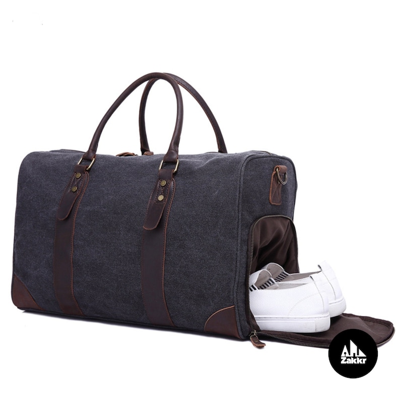 Pu&ograve; includere: Una borsa da viaggio in tela grigia con dettagli in pelle marrone e uno scomparto per le scarpe con cerniera. La borsa ha due manici superiori e una chiusura con cerniera. La borsa &egrave; aperta e si pu&ograve; vedere un paio di scarpe bianche all'interno dello scomparto per le scarpe.