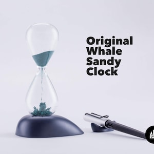 May include: A blue hourglass with a whale-shaped base sits on a white surface. The hourglass is filled with blue sand and has a silver metal frame. The text "Original Whale Sandy Clock" is printed in black on a white background. A silver pen with a black tip is lying on a black surface next to the hourglass. The pen has a small black logo with the text "Zakkr" printed on it.