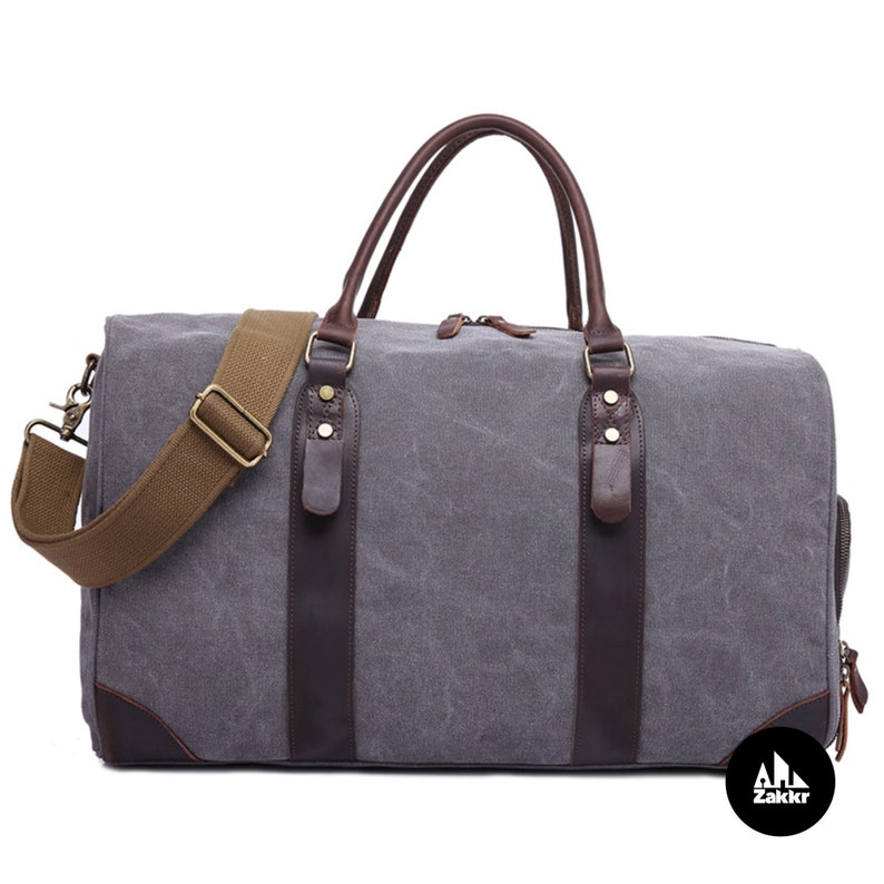 Pu&ograve; includere: Una borsa da viaggio in tela grigia con dettagli in pelle marrone e una tracolla regolabile marrone. La borsa ha due manici superiori e una chiusura a zip.
