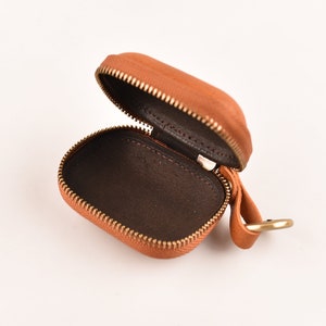 May include: A small, brown leather case with a zipper closure and a gold metal loop. The case is open and the inside is lined with brown fabric.