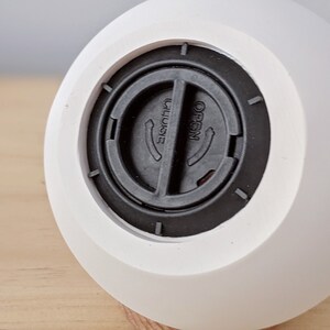 May include: White ceramic diffuser with a black plastic lid. The lid has a round opening with the words "OPEN" and "CLOSE" printed on it.